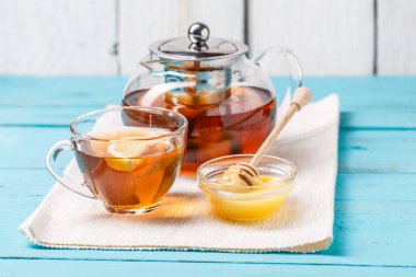 Bir bardak limonlu çay, cam çaydanlık ve mavi ahşap masada bal..