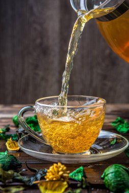 Kurumuş çiçeklerle dolu yeşil çay sürahisinden bardağa döküldü