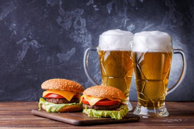 İki hamburger resmi, ahşap masada biralı bardaklar.