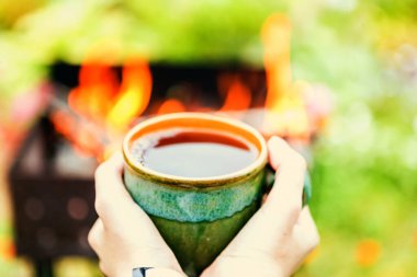 Elleri çay fincanı, brazier ve arkasında ateş tutuyordu.