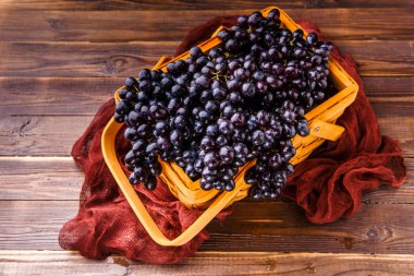 Yukarıdan görüntü: Tahta sepetteki siyah üzümler, stüdyodaki masada kırmızı bez.