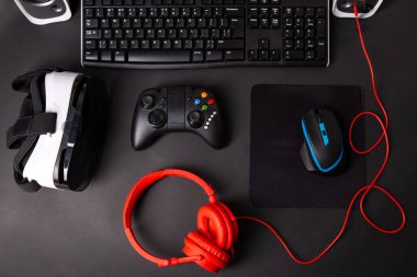 Top view a gaming gear, mouse, keyboard, joystick, headset, VR Headset on black table background. Gamer workspace concept. clipart