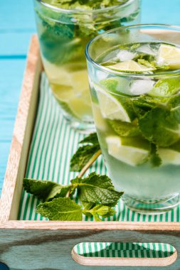 Mavi ahşap masada naneli iki bardak mojito.