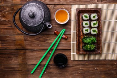 Çaydanlıklı çay, ahşap masada bambu peçetenin üstünde rulo.