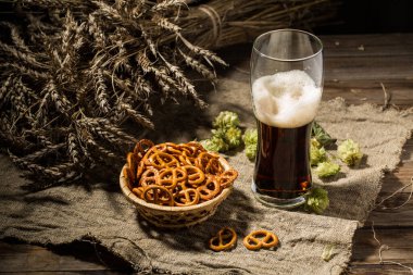 Buğday ve zıpzıp dolu cam bira, ahşap masada keten kumaş üzerinde kraker sepeti