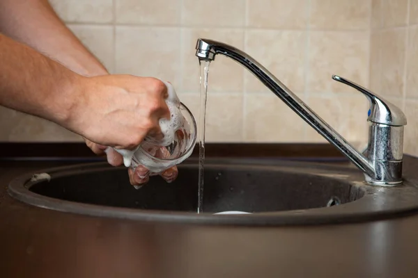 照片上的人的手一边在厨房的水池里洗透明的杯子 — 图库照片