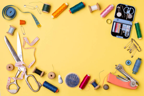 Composition with threads and sewing accessories - scissors, centimeter, pins on yellow background. Concept for needlework and tailoring