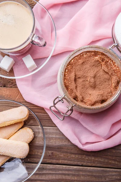 Tiramisu, coffee , savoiardi on pink tissue on brown wooden table