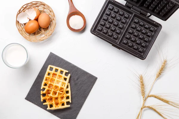 Photo on top of flour, eggs, waffle iron, spikes, fresh roasted waffles on white table