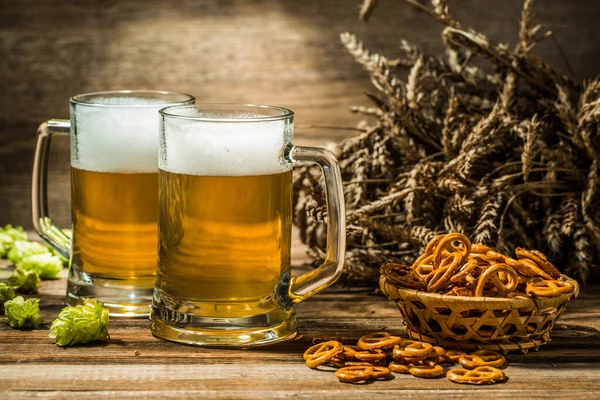 Two tankard beer with wheat and hops , basket of pretzels on wooden table