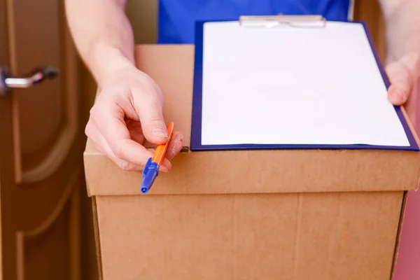 Photo close up of courier with pen, blank sheet of paper, cardboard box in apartment