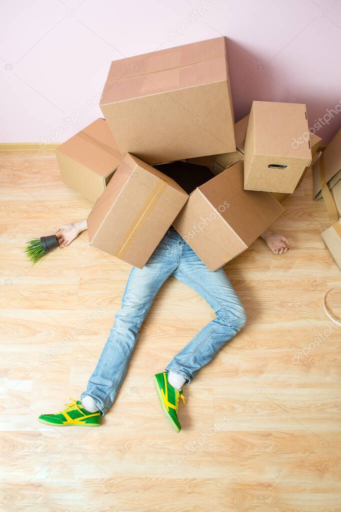 Photo of man in jeans lying under cardboard boxes in new apartment