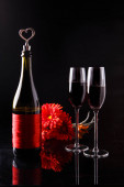 Láhev vína se zátkou ve tvaru srdce a dvě sklenice tří červených gerber. Romantický večer. Svatý Valentýn