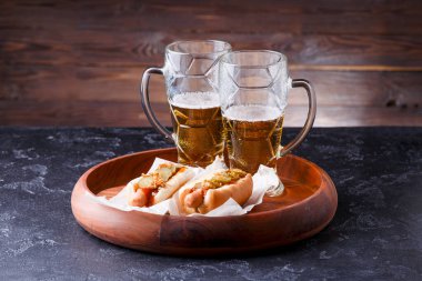 İki kupa bira ve ahşap arka plandaki ahşap tepside sosisli.