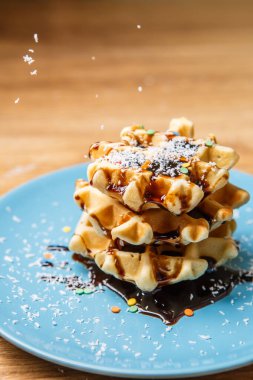 Ev yapımı waffle Çikolata ve hindistan cevizini mavi tabağa serpiyor