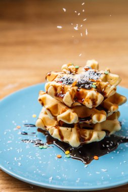 Ev yapımı waffle Çikolata ve hindistan cevizini mavi tabağa serpiyor