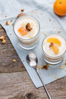 Bisküvi, yoğurt, mandalina ve cevizli taze ev yapımı tatlı, ahşap arka planda sunulan bir bardakta servis edilir.