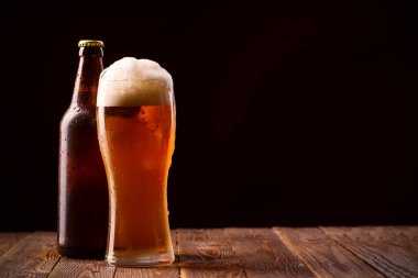 Fotoğraf: Butttle ve bir bardak bira masada ve siyah arka planda.