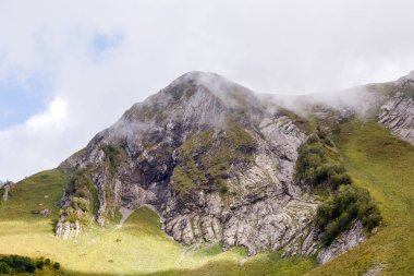 Dağlık yamaçların fotoğrafı, bitki örtüsü ve yaz günü bulutlu gökyüzü.
