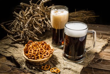 Kupa ve cam bira, bir sepet kraker ve ahşap arka planda keten kumaş üzerinde buğday.