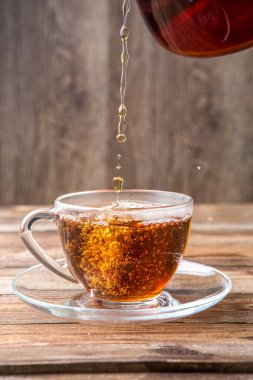 Çay şeffaf bardakta, çay tabağı ahşap masada duruyor.