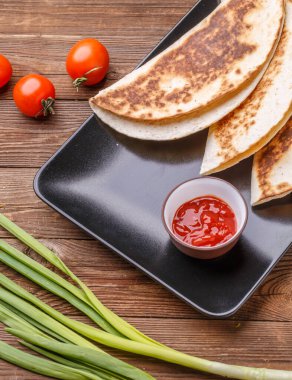 Tavuklu tortilla, ahşap masada siyah tabakta domates.