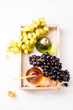 Yeşil ve siyah üzümlü ahşap tepsinin üstünden görüntü, siyah arka planda saman bulunan iki şişe meyve suyu