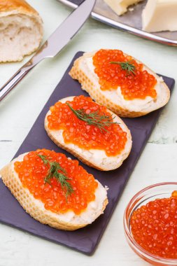 Beyaz ahşap masada kırmızı havyarlı baget ekmeğinin fotoğrafı.