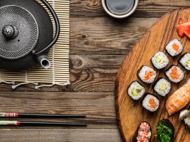 Japon deniz ürünleri suşisi, rulo rulo ve çaydanlık ahşap yüzeyde servis edilir.