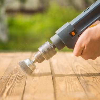 Elektrikli fırça metal diski olan elleri zımparalayan bir adam. Açık havada ahşap işçiliği.