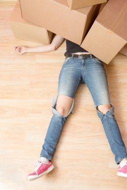 Yeni dairede karton kutuların altında yatan kot pantolonlu bir kadın resmi