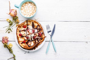 Kahvaltıda üstünde krep, üstünde çikolata, dondurma ve kakao olan bir fotoğraf.