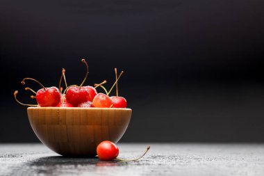 Gri masadaki ahşap bardakta tatlı vişne resmi.