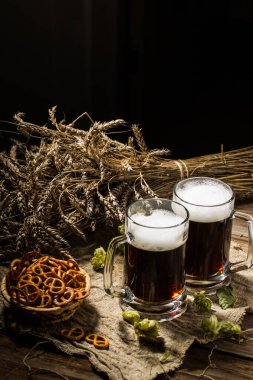 Buğday ve zıpzıp dolu iki tankard birası, ahşap masada bir sepet kraker.