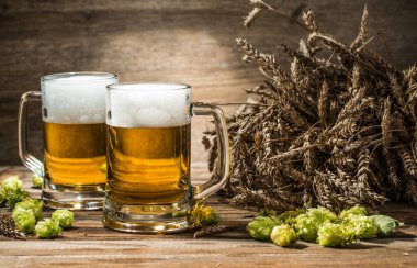 Masada iki kupa bira ve boş ahşap arka planda buğday.