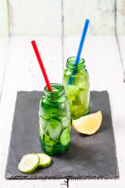 Beyaz ahşap masada salatalık ve limonlu iki şişe detoks diyeti ferahlatıcı su.