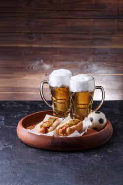 İki kupa bira ve ahşap arka plandaki ahşap tepside sosisli.