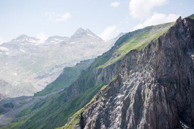 Dağlık yamaçların fotoğrafı, bitki örtüsü ve yaz günü bulutlu gökyüzü.