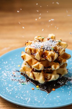 Ev yapımı waffle Çikolata ve hindistan cevizini mavi tabağa serpiyor