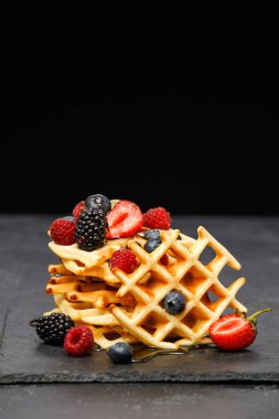 Böğürtlenli taze Viyana waffle 'larının fotoğrafı stüdyoda boş bir arkaplanda tahtaya bal döküyor.