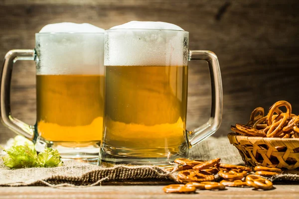 Zwei Bierkrüge Mit Hopfen Und Brezeln Auf Leinentuch Auf Holztisch — Stockfoto