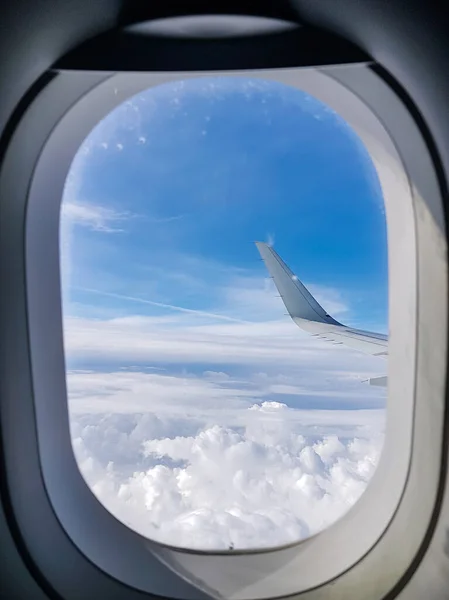 Image of airplane wing, cloudy sky from porthole in afternoon