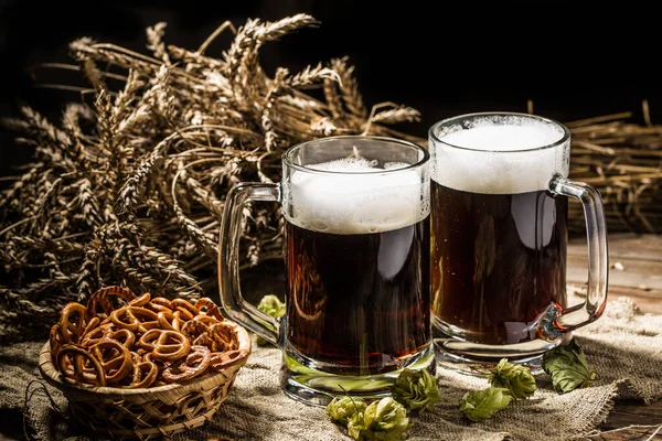 Couple beer mug with hop and pretzels on linen cloth on wooden table