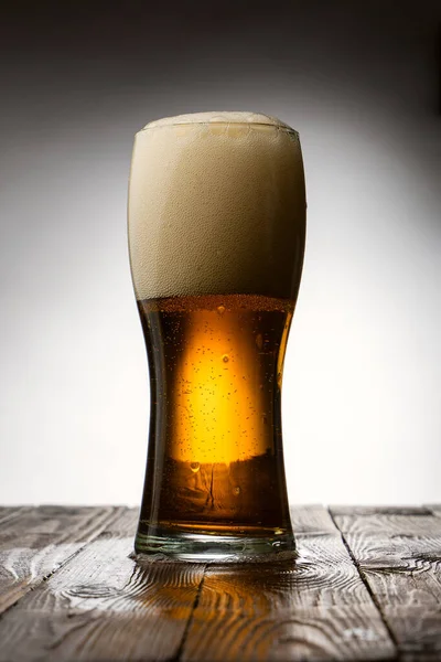 Frosted glass of light beer on wood table and gray background behind