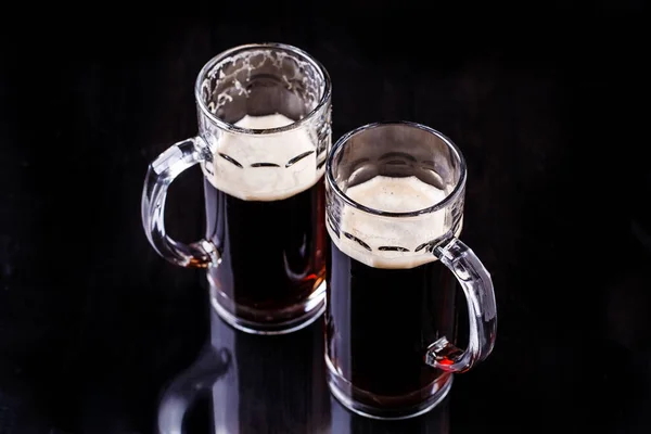 Two mugs of foamy beer on black background