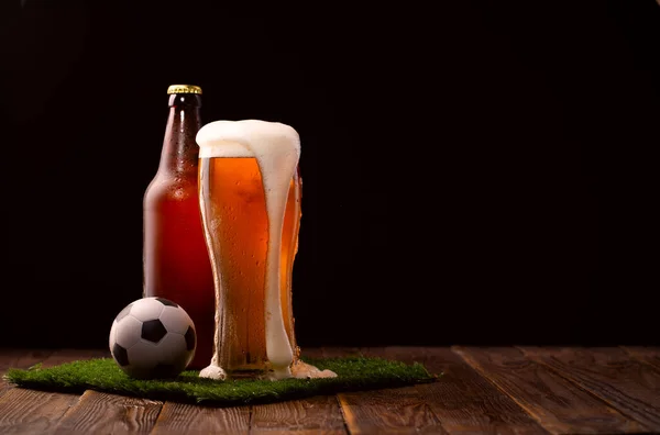 Photo of buttle and glass of beer, soccer ball on green grass at table