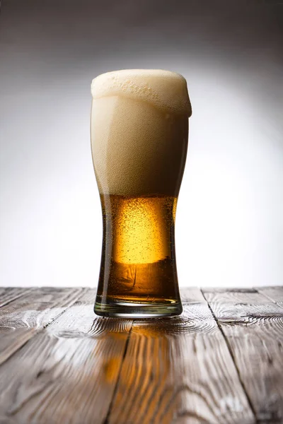 Frosted glass of light beer on wood table and white background behind