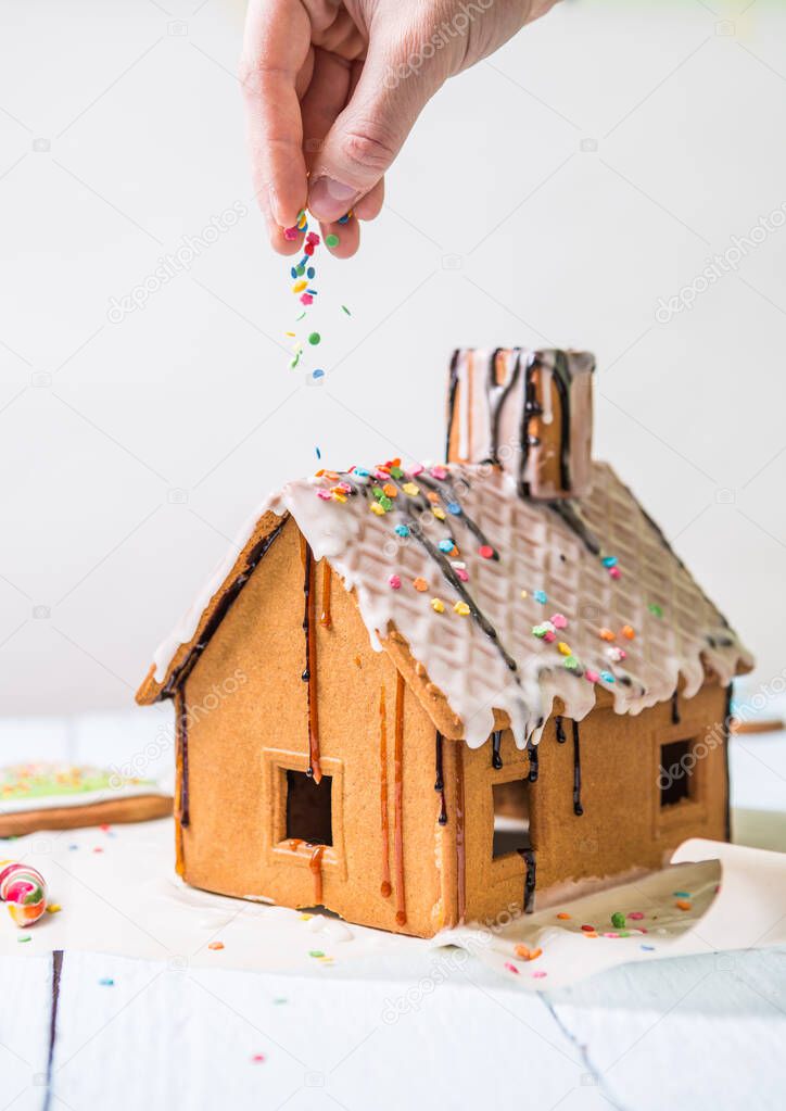 Man sprinkles Homemade gingerbread house confectionery sprinkling on white background