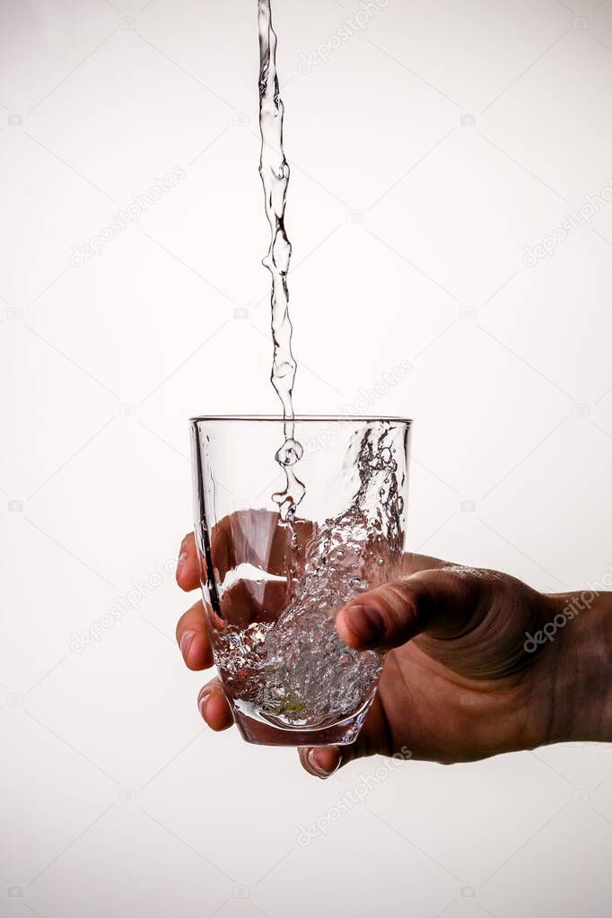 Image of hand with glass in which water flows on empty gray background