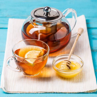 Bir bardak limonlu çay, cam çaydanlık ve mavi ahşap masada bal..